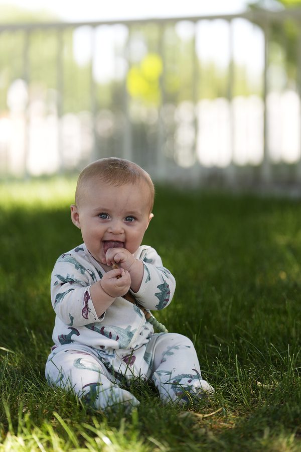 Baby sitting in the grass, laughing, with a teething toy
