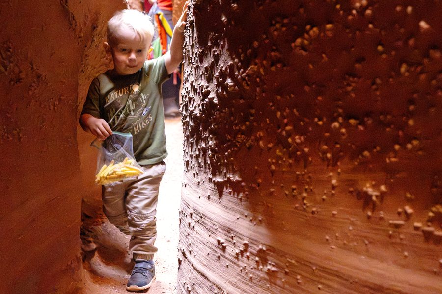 Little boy with a bag of snacks walking through a red rock slot canyon