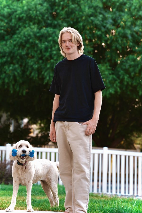 Senior portrait of a young man with his golden doodle holding a blue bone